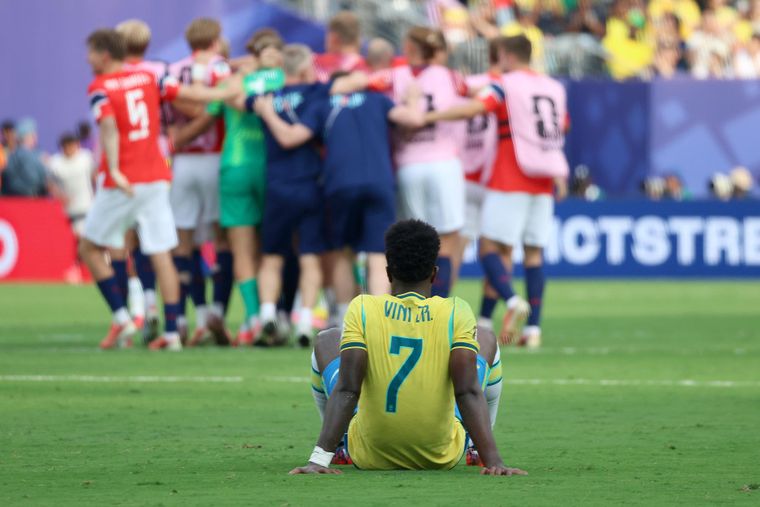 Vinicius Júnior tirado en el suelo mientras los jugadores de Noruega festejan haber eliminado a Brasil.