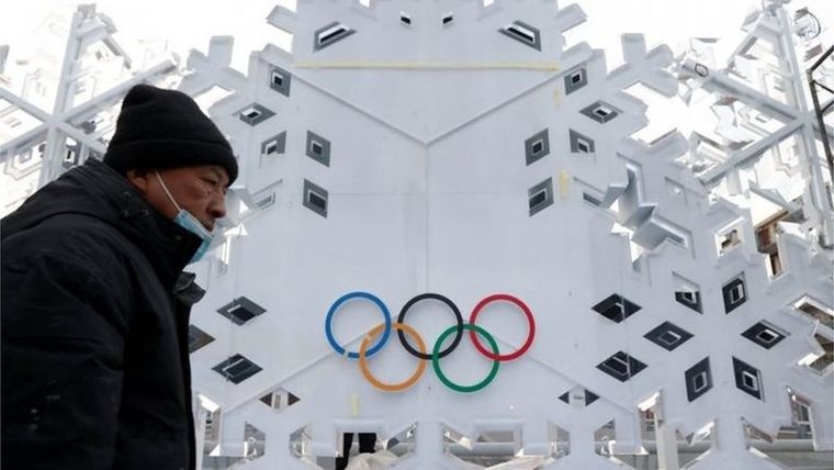 Un hombre con mascarilla y abrigo camina frente a un edificio con el logo olímpico. Foto: REUTERS
