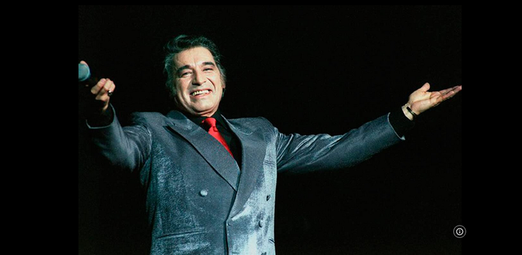 El cantante Sandro sobre un escenario con un gesto a su público. Foto: https://www.imdb.com/name/nm0762275/mediaviewer/rm1162611712/