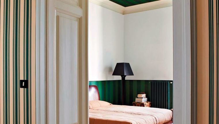 En la imagen el método sándwich representado en una habitación con un verde fuerte y estampado en las partes superior (techo) e inferior (empapelado) con un contraste brillante y claro en la pared, cama y puerta. Foto: Farrow & Ball
