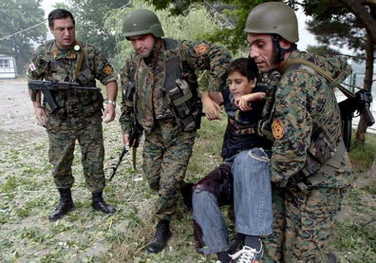 Tres soldados recogen a un niño herido en Gori tras el ataque de aviones rusos. Foto: EFE