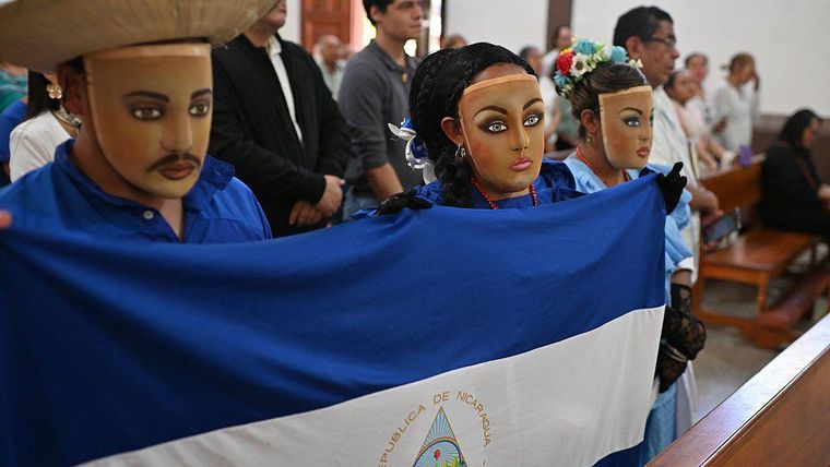 Nicaragüenses en el exilio con el rostro cubierto, sosteniendo una bandera nicaragüense, asisten a misa en la Iglesia de San Francisco en San José, Costa Rica, el 19 de abril de 2026