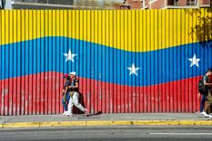 Dos personas caminan delante de una bandera de Venezuela, país castigado por el poder de Estados Unidos. Foto Dpa&nbsp;