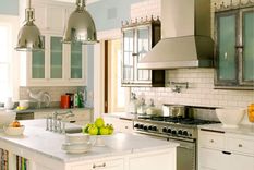 Cocina con gabinetes blancos, isla de cocina blanca con un par de luces colgantes plateadas, pintura azul claro en las paredes. Foto: Benjamin Moore.