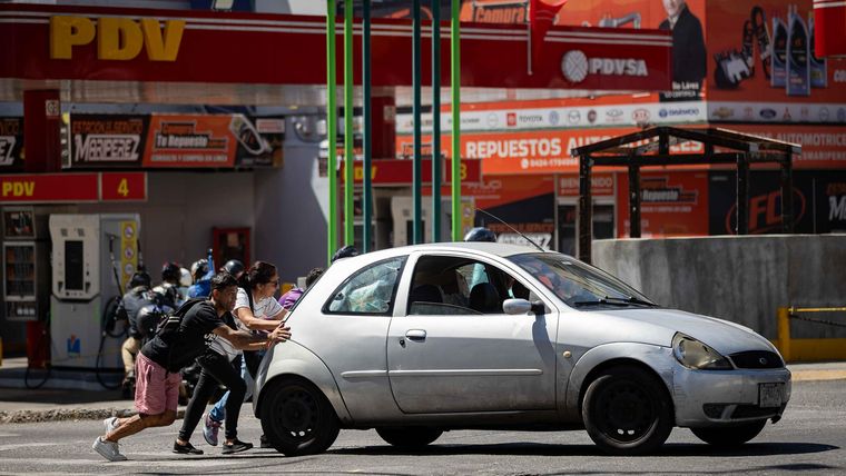 Personas empujan un auto frente a una estación de servicio de la estatal Petróleos de Venezuela. Personas empujan un auto frente a una estación de servicio de la estatal Petróleos de Venezuela.