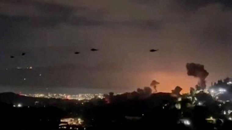 Helicópteros militares estadounidenses sobrevuelan Caracas, con columnas de humo claramente visibles provenientes de los ataques aéreos anteriores.