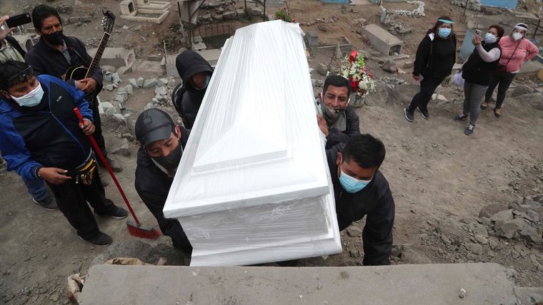 Operarios de un cementerio en Lima (Perú) cargan el ataúd de un fallecido por covid-19. Foto: RT