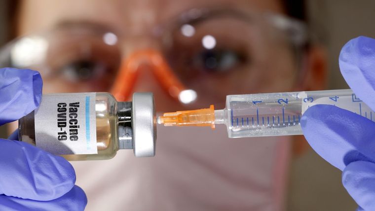 Una mujer sostiene un frasco que simula una vacuna contra el covid-19 y una jeringa médica.