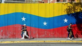 Dos personas caminan delante de una bandera de Venezuela, país castigado por el poder de Estados Unidos. Foto Dpa&nbsp;