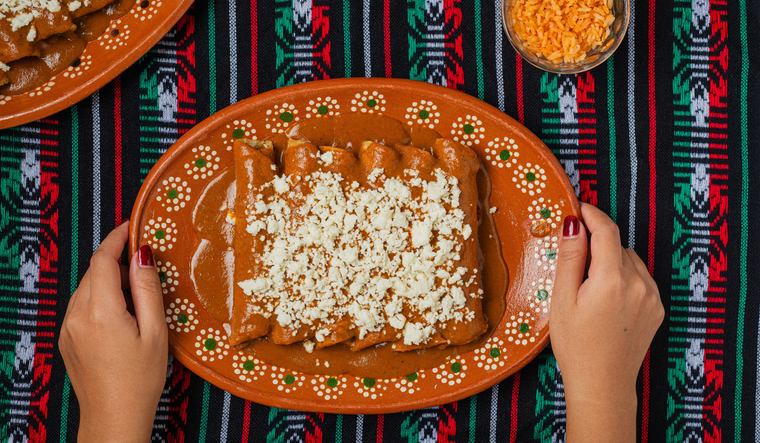 Aunque hoy se sirven en platos abundantes, la receta original de enchiladas rojas surgi&oacute; como una comida econ&oacute;mica y r&aacute;pida para las familias trabajadoras, consolid&aacute;ndose como un s&iacute;mbolo de la gastronom&iacute;a mexicana.