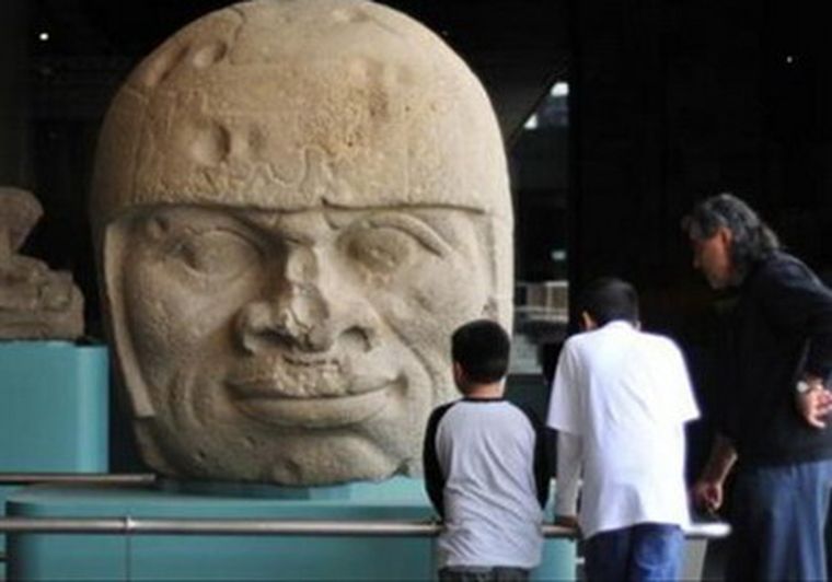 Unas personas observan, la figura Cabeza colosal