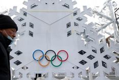 Un hombre con mascarilla y abrigo camina frente a un edificio con el logo olímpico. Foto: REUTERS