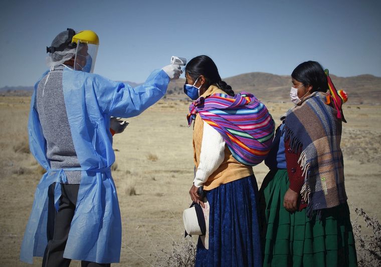 Un hombre toma la temperatura a mujeres de las comunidades altoandinas Quechuas antes de ingresar a una feria rural el 8 de julio de 2020 en la localidad de Coata, a unos cuarenta minutos de la ciudad de Puno (Perú).