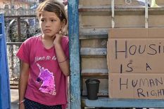 Foto: GETTY IMAGES. La vivienda es un derecho humano, reza el cartel junto al que está está niña refugiada en Grecia.