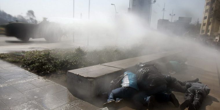Manifestantes en Santiago de Chile se protegen en el suelo de un carro lanzaaguas. Foto: EFE