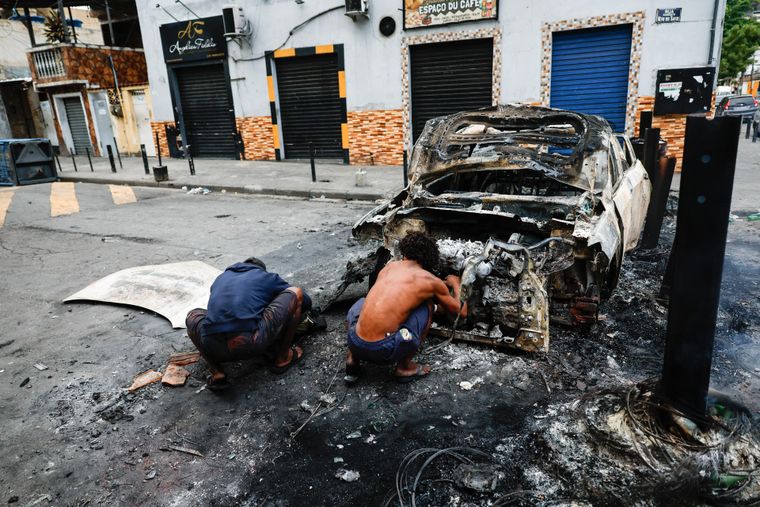 Personas se cubren detrás de un vehículo incinerado durante el operativo policial en Río de Janeiro