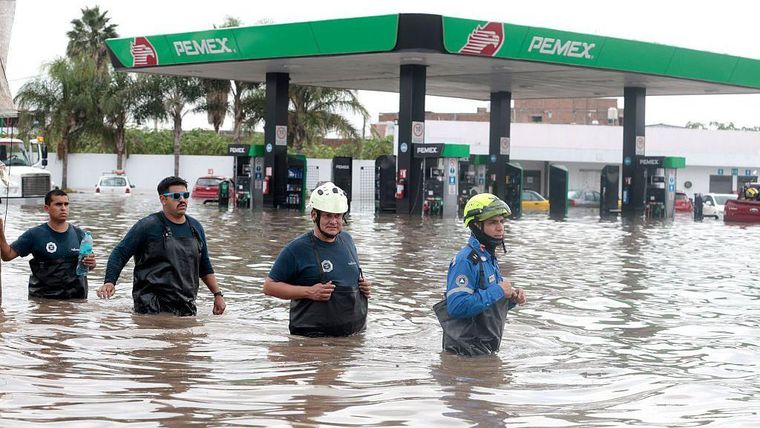 Bomberos caminan por una calle inundada después de que las fuertes lluvias provocaran el desbordamiento del río Arroyo Seco en Tlajomulco de Zúñiga, Jalisco.