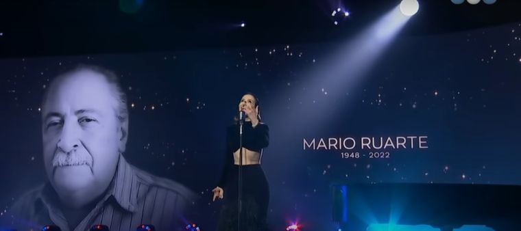 Natalia Oreiro canta en el homenaje a los artistas fallecidos. El mendocino Mario Ruarte, en la imagen de atrás. Foto: Imagen de tv.