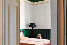 En la imagen el método sándwich representado en una habitación con un verde fuerte y estampado en las partes superior (techo) e inferior (empapelado) con un contraste brillante y claro en la pared, cama y puerta. Foto: Farrow & Ball
